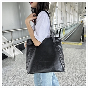 Detail of black faux leather tote bag with geometric patchwork and long shoulder straps