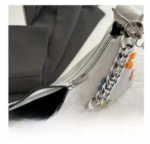 Detail of silver zipper and colorful crochet flowers on white croc-embossed bag