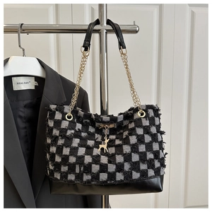 Detailed macro view of the tweed checkerboard texture and golden deer charm on tote bag