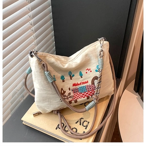 Detailed embroidery of cats and trees on cream canvas bag with woven rope strap