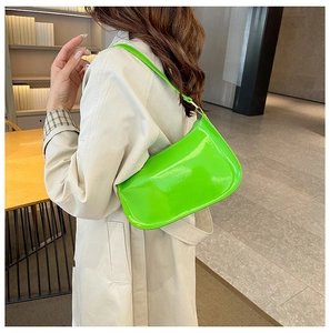 Dettaglio di una borsa sottobraccio in pelle verniciata verde neon indossata con un trench