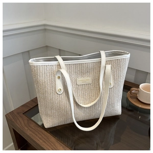Close-up of woven straw tote bag featuring a leather logo patch and gold rivet details