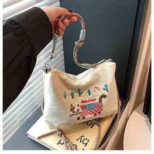 Close-up of cat embroidery and braided rope strap on beige canvas tote bag