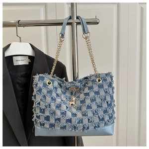 Detail of denim checkered tote bag with gold chain strap and deer charm accessory