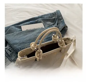 Close-up of cream handbag with floral embroidery and woven rope handle with tassel detail