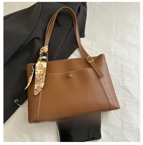 Detail of brown tote bag featuring textured PU leather, adjustable strap, and printed silk scarf