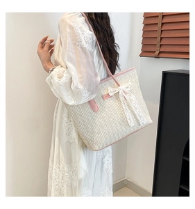 Détail du sac cabas en paille avec anses en cuir rose et décoration de nœud en dentelle