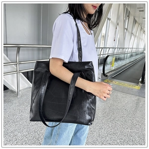 Detail of a large black textured leather tote bag with dual shoulder straps worn by model