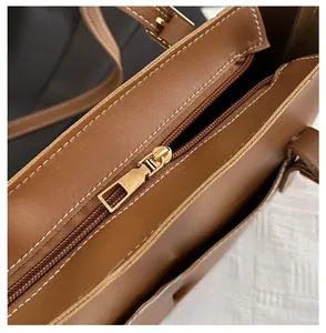 Close-up of smooth gold-tone zipper on brown leather tote bag with white stitching