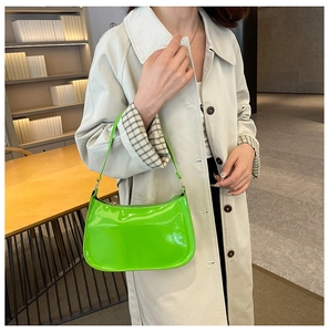 Borsa baguette in vernice verde fluorescente indossata su un trench beige
