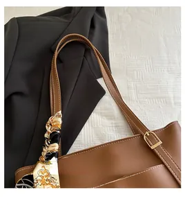 Detail of a brown leather tote bag handle with decorative printed silk scarf and gold hardware