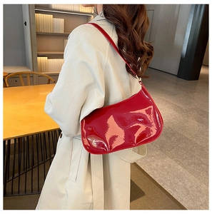 Borsa sottobraccio in vernice rossa lucida portata a spalla su sfondo neutro