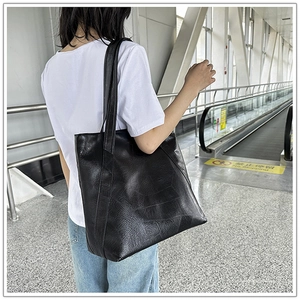 Outdoor lifestyle view of large black leather tote bag worn on shoulder by a model