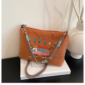Detailed view of colorful cat embroidery on a large orange canvas crossbody shopping bag