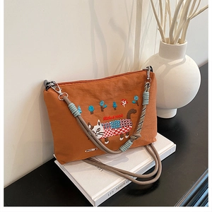 Detailed cat embroidery and woven rope strap on an orange canvas crossbody bag