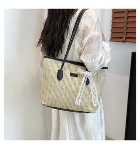 Détail du sac cabas en paille avec anses en cuir noir et décoration de nœud en dentelle