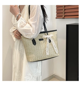 Détail du sac cabas en paille beige avec anses en cuir noir et nœud en dentelle blanche