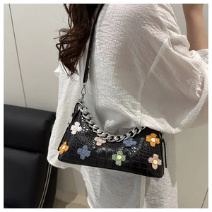 Close-up of black crocodile pattern baguette bag with colorful velvet flower charms