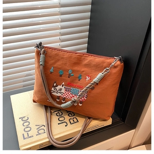 Close-up of cat embroidery and braided rope strap on brown crossbody handbag