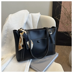 Detail of black PU leather tote bag featuring contrast stitching and floral silk scarf charm