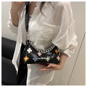 Detail of black crocodile texture baguette bag with colorful plush 3D flower charms