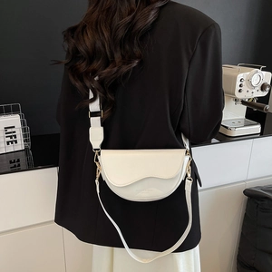 Chic beige half-moon saddle bag with wide woven strap and gold hardware worn by model