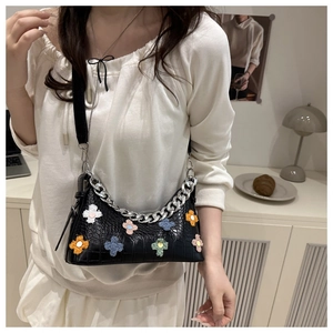 Detail of black croc-effect baguette bag with colorful plush flowers and silver chain