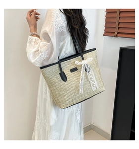 Détail du sac cabas en paille tissée avec anses en cuir noir et nœud en dentelle