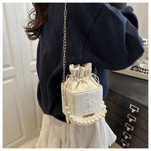 Detail of white bucket bag featuring pearl handle, gold chain and snake skin texture