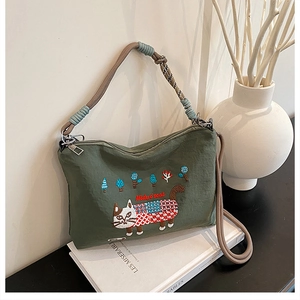 Close-up of green canvas bag featuring detailed cat embroidery and braided rope handles
