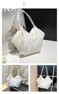 Detail of white quilted tote bag featuring colorful wavy embroidery and wide textile strap