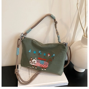 Close-up of green canvas bag featuring detailed cat embroidery and braided rope strap