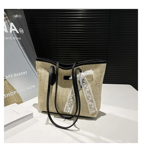 Détail du sac cabas en paille tissé à la main avec un nœud en dentelle blanche et cuir noir
