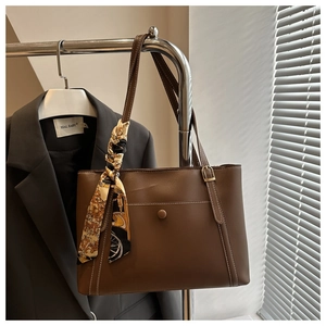 Detailed view of brown leather tote bag with white stitching and floral silk scarf handle