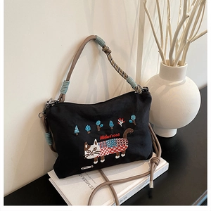 Detail of black canvas bag with cat embroidery and woven cord handles in a still life setting