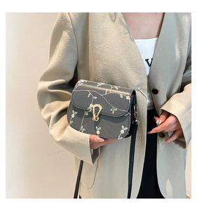 Détail du sac selle gris avec broderie florale et fermoir doré sur un blazer beige