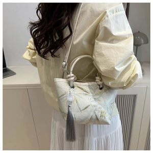 Detail of embroidered crossbody bucket bag with elegant long tassel and metal handle