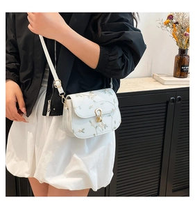 Détails de broderie florale et fermoir doré sur un sac bandoulière crème élégant