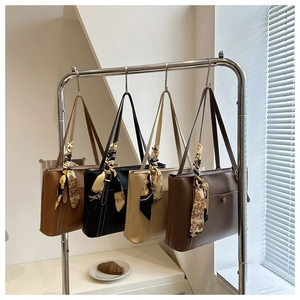 Detail view of four leather tote bags in various colors hanging on a rack with silk scarves