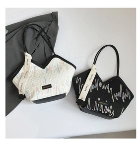 Detail of V-shaped tote bag with wavy embroidery and branded woven strap accent