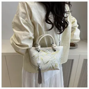 Close-up of beige silk fabric handbag featuring gold bamboo leaves and grey tassel charm