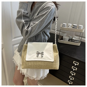 Detail of summer straw bag featuring a silver metal bow buckle and elegant chain strap