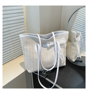 Détail d'un sac cabas en paille avec garniture en similicuir blanc et nœud en dentelle