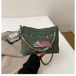 Close-up of dark green canvas bag featuring detailed cat embroidery and braided strap
