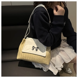 Detail of woven straw shoulder bag with silver bow clasp and chain strap on model
