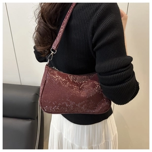 Detail of burgundy snakeskin embossed shoulder bag worn by model showing actual scale