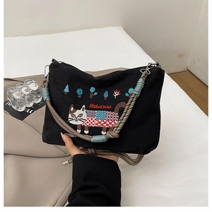 Close-up of cat embroidery and colorful braided strap on a black canvas crossbody bag