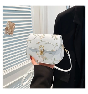 Détail d'un sac selle blanc avec broderie florale en dentelle et fermoir doré fer à cheval