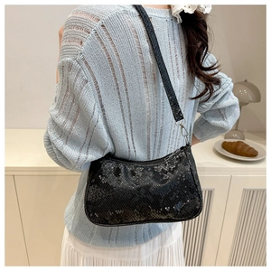 Gros plan du sac à bandoulière noir à motif serpent porté avec un pull en maille bleu