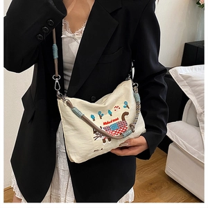 Detail of embroidered cat pattern on white canvas bag with mixed material strap